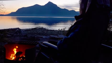 woman watches sun setting in the glow of a campfire