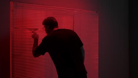man peeking through red lit blinds