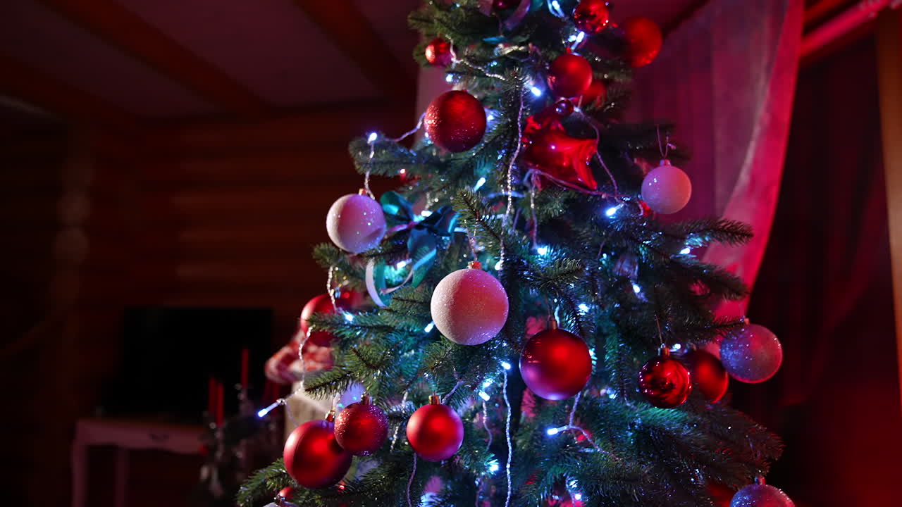 Beautiful Christmas tree with lights and ribbons. Amazing fir tree decorated with Christmas balls near the cozy fireplace in the living-room.