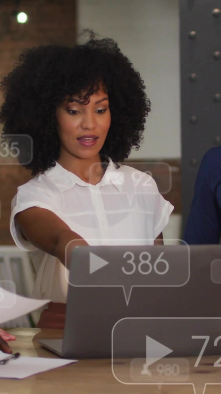 Vertical video: Team handing docs sparking woman pointing, tapping laptop, reviewing tech UI badges