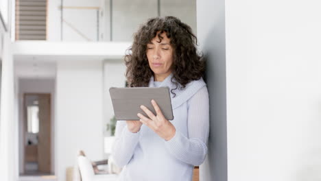 Glückliche-Reife-Kaukasische-Frau,-Die-Sich-Zu-Hause-Mit-Einem-Tablet-An-Die-Wand-Lehnt,-Zeitlupe