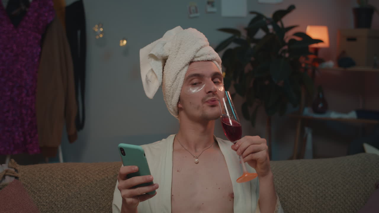 Person with towel on head, eye mask, wine, and phone