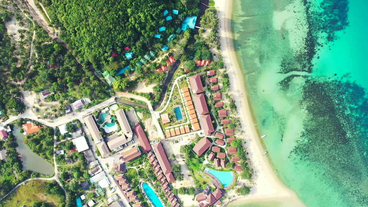 Holiday resort with bar restaurants and villas on white sandy beach of tropical island, in front of turquoise calm lagoon in Thailand