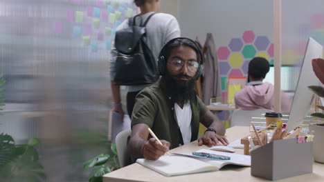 young indian businessman using computer brainstorming browsing online research ideas for startup company project networking reading email listening to music in busy modern office workplace