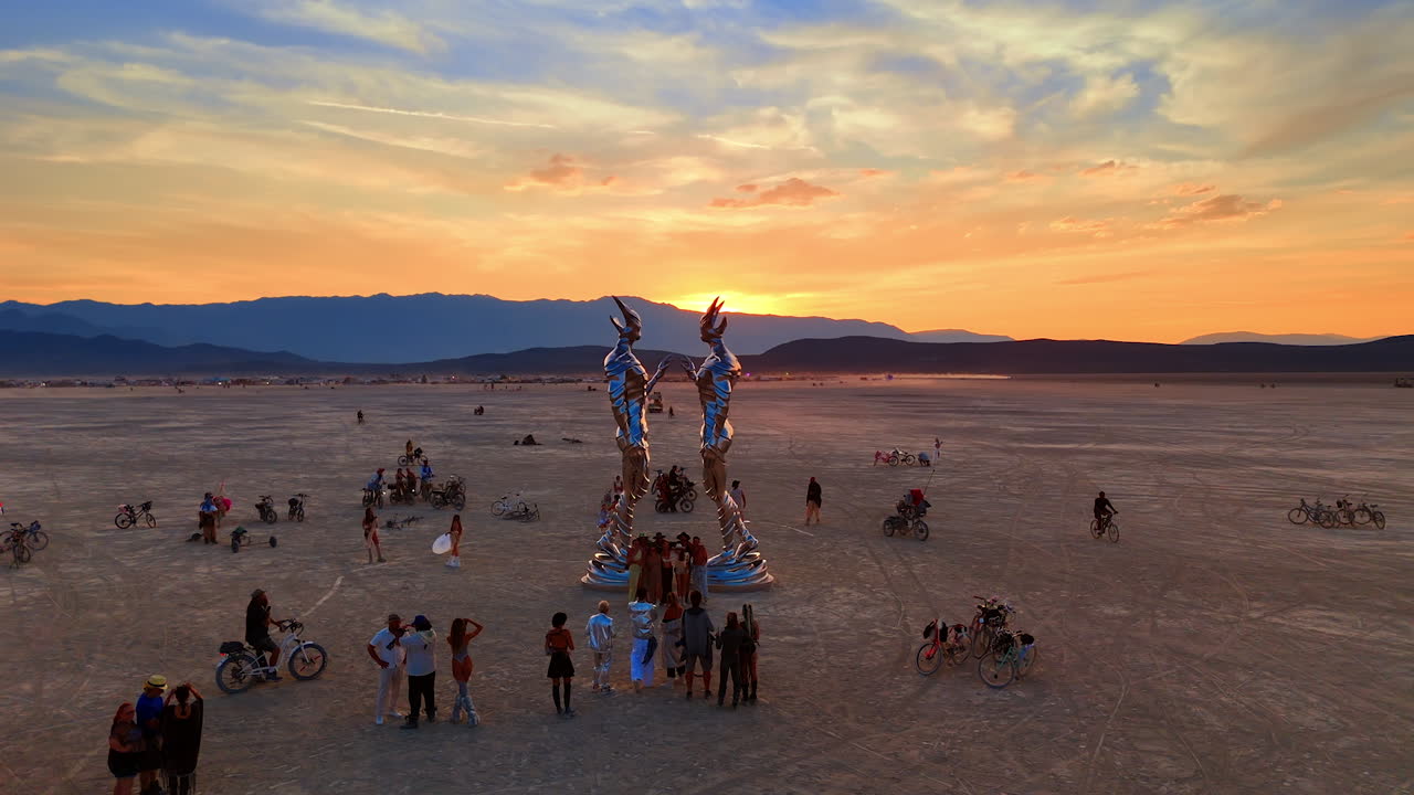 Nevada, USA, 25 August 2025: Drone shot of people gathering around a tall metallic art sculpture at Burning Man during a vibrant sunset