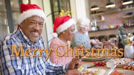 Animation-of-merry-christmas-text-over-diverse-senior-friends-at-christmas-dinner-at-home