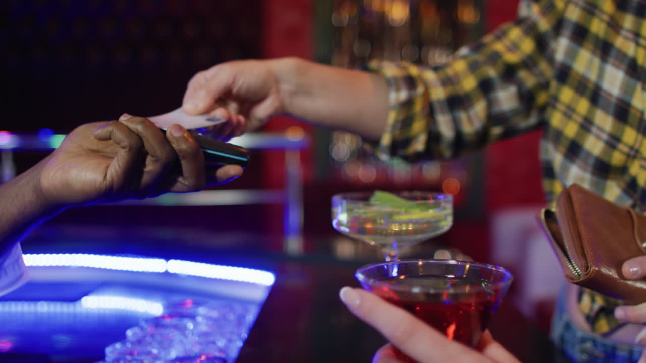 video di una sezione centrale di diversi barman e clienti femminili che pagano le bevande con carta di credito al bar