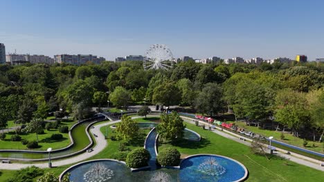 aerial view over oraselul copiilor park with an artesian fountain and a white ferris wheel surrounded by lush vegetation, bucharest, romania