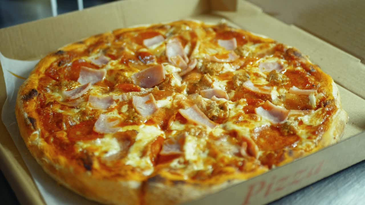 Cutting cooked Italian pizza and adding parsley spices inside box by worker