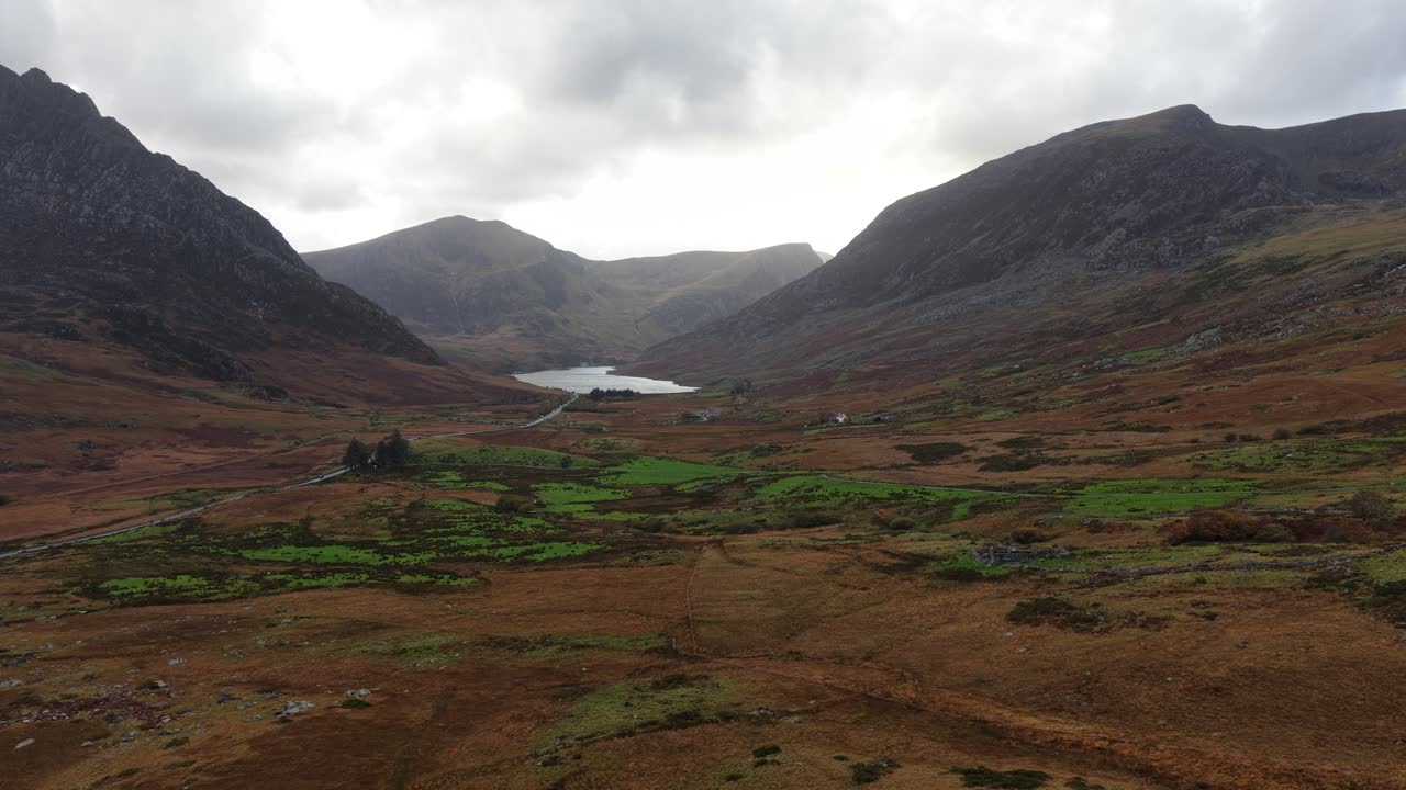 Aerial drone video of the Ogwen Valley in Snowdonia National Park, showcasing rugged terrain, open fields, and the dramatic highland mountains of North Wales