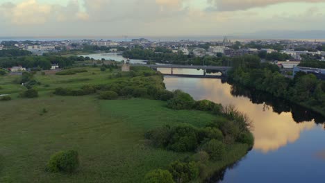 las aguas tranquilas del río corrib reflejan luz dorada en las nubes por el castillo de terryland en galway, irlanda.