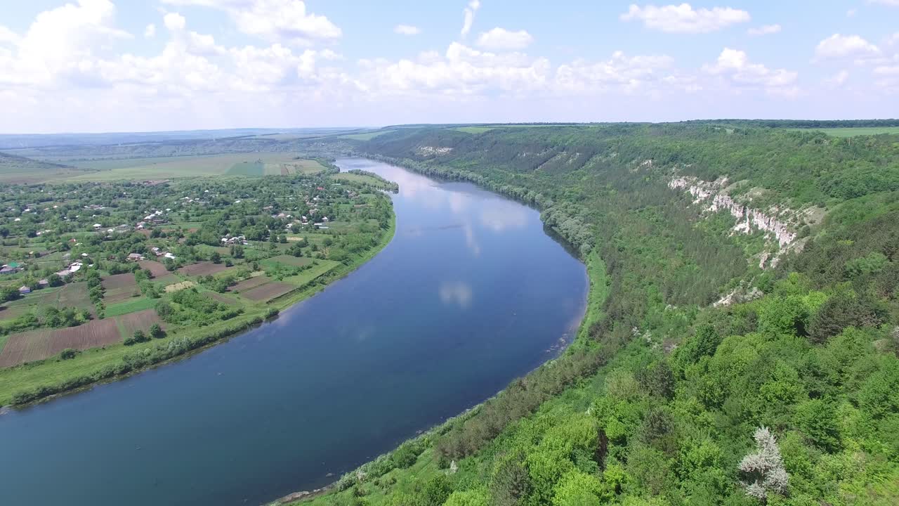 A wide blue river flows between rocks with trees and countryside with long fields and a private sector. Aerial view.