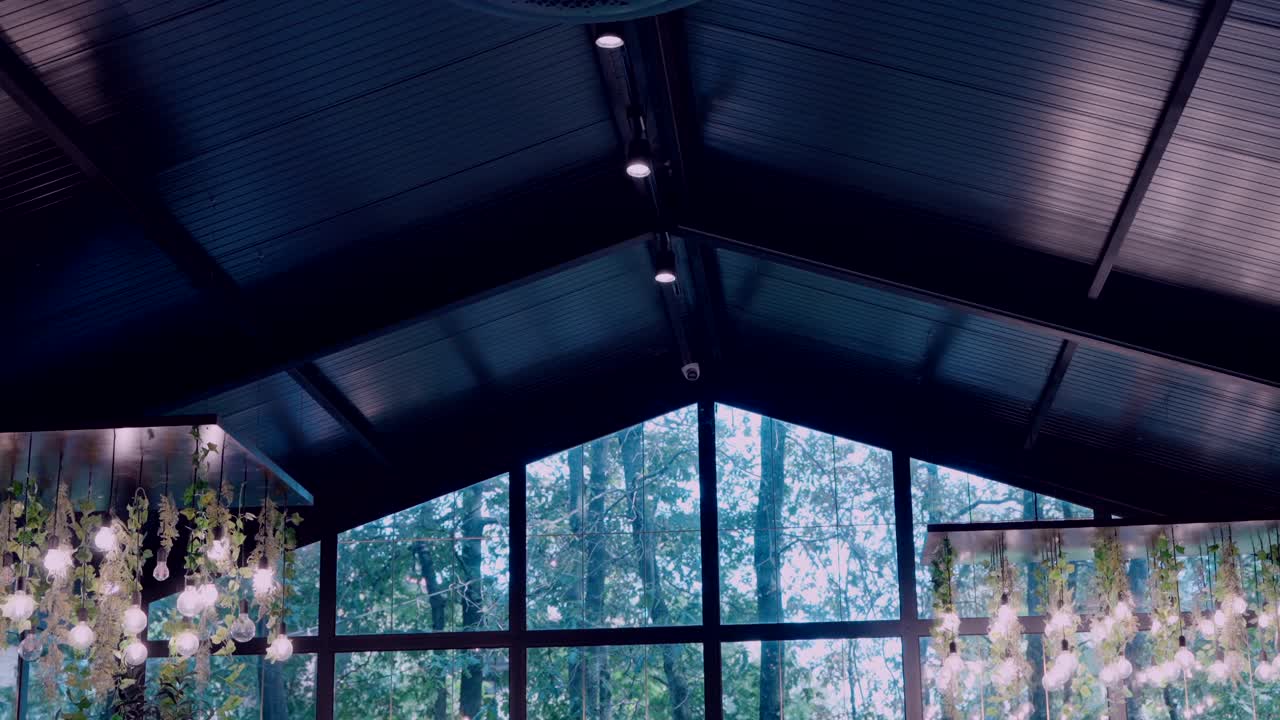 Black metal ceiling with spotlights and hanging floral lights in a glass hall.