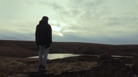 young boy standing and looking out on to the winter landscape, with moorlands, fens, a lake and stormy winters sky