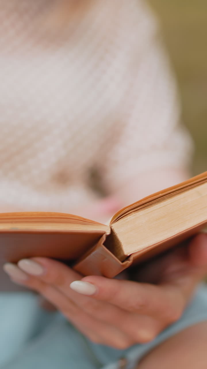 primer plano de manos volviendo páginas en un libro abierto, enfoque suave en pantalones cortos azules y uñas delicadas momento de lectura al aire libre pacífico con un fondo natural borroso