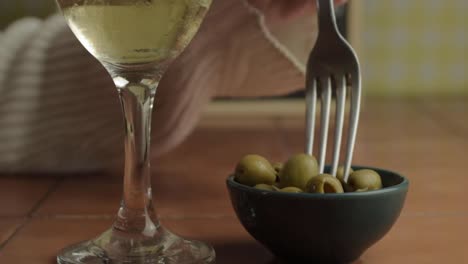 hand mit einem glas weißwein, der grüne oliven mit einer gabel isst