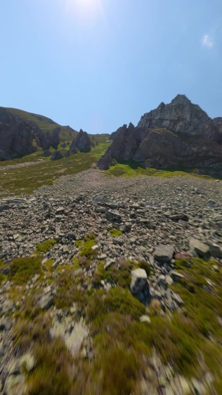 Drone FPV cattura un video verticale dinamico sorvolando montagne aspre, pendii rocciosi e valli verdi a Puerto San Isidro, Asturie