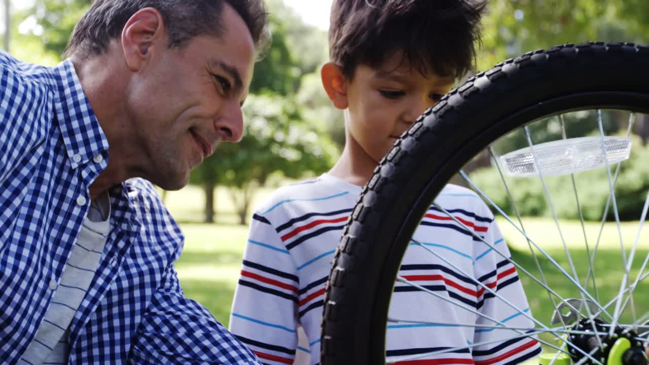 hijo y padre reparando su bicicleta en el parque