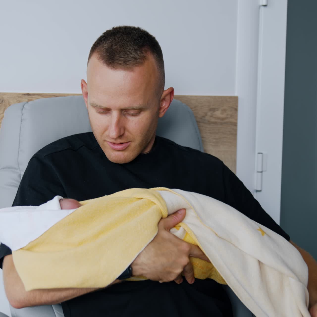 Happy father sits in armchair holding his newborn baby. New-made parent taking care of a child after birth in hospital