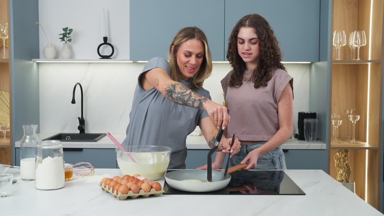 Young mother teaching her teenage daughter to flip pancakes
