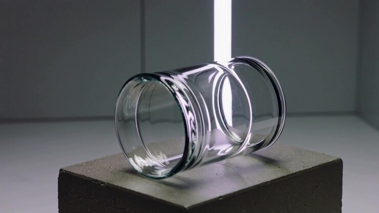 Striscia LED che appare dietro un barattolo trasparente su un blocco di cemento, creando riflessi e mostrando un'asta viola.