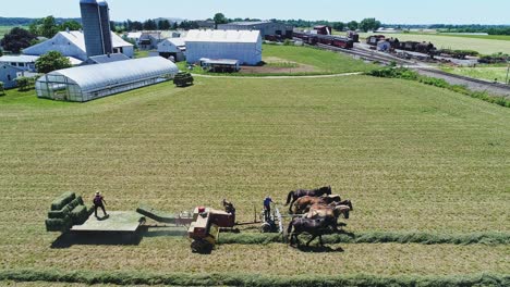 an aerial view of an amish farmers with five horses harvesting his crops and loading them on to a cart looking over the countryside on a beautiful day