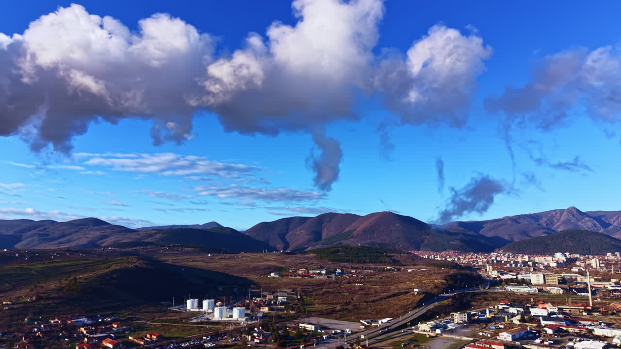 Il fumo si alza dalle fabbriche vicino alle montagne di giorno in una zona rurale con cielo azzurro e nuvole