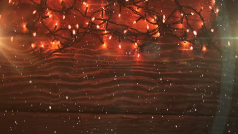 animation of snow falling over red christmas fairy lights on wood