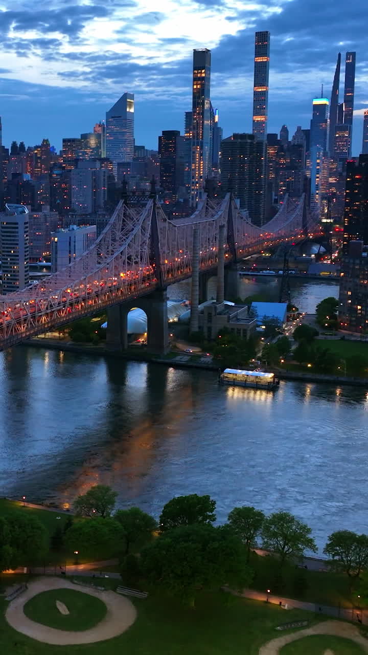 New York in lights at evening time. Beautiful Queensboro Bridge with green park and parking lot under. View from top. Vertical video