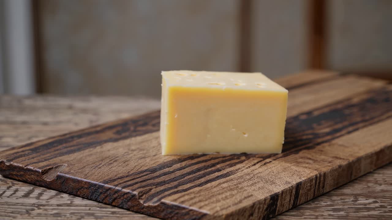 Close-up video shot of a cheese block on a rustic wooden board, showcasing texture and detail