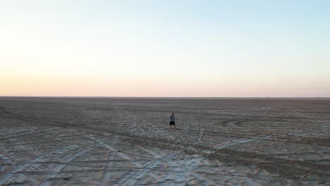 Vista-Aérea-De-La-Figura-Masculina-Caminando-En-Un-Enorme-Campo-De-Salinas-Bajo-El-Sol-Del-Atardecer