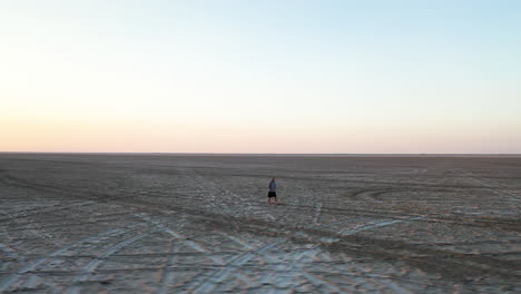 Aerial View of Male Figure Walking on Massive Salt Flats Field Under Sunset Sun