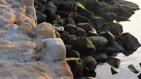 caminar a lo largo de la costa de la isla, puesta de sol cerca de la superficie del agua y el camino de piedra costera, reflejo del sol, paisaje natural idílico y pacífico por la noche