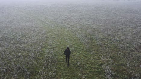 Lonely-Man-in-Dark-Clothes-Walking-in-Fog-on-Meadow-at-Early-Morning-Aerial-View