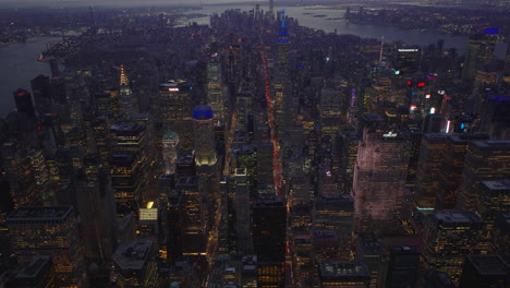 High-angle-view-of-long-straight-avenues-passing-city-district-between-high-rise-buildings.-Tilt-up-reveal-of-city-panorama-at-dusk.-Manhattan,-New-York-City,-USA