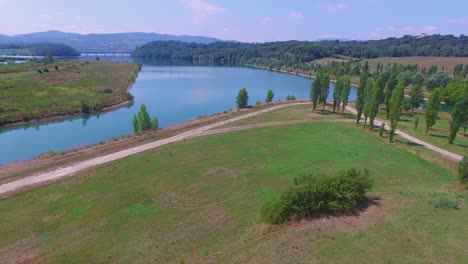 fields of tuscany on the banks of the serchio river near a traffic bridge during a sunny day, aerial lift pedestal shot