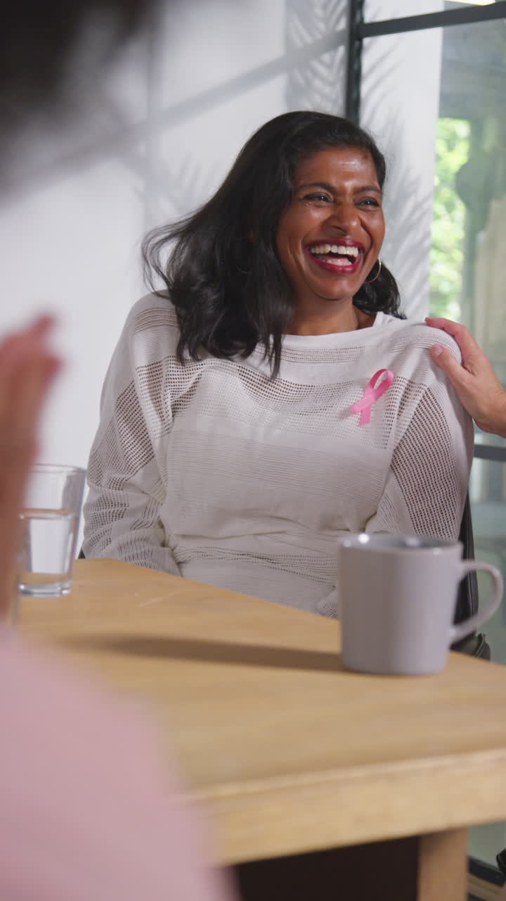 Vertical Video Of Smiling Mature Woman Wearing Pink Breast Cancer Awareness Ribbon Meeting And Talking At Therapy Support Group For Cancer Treatment Patients With Counsellor 1