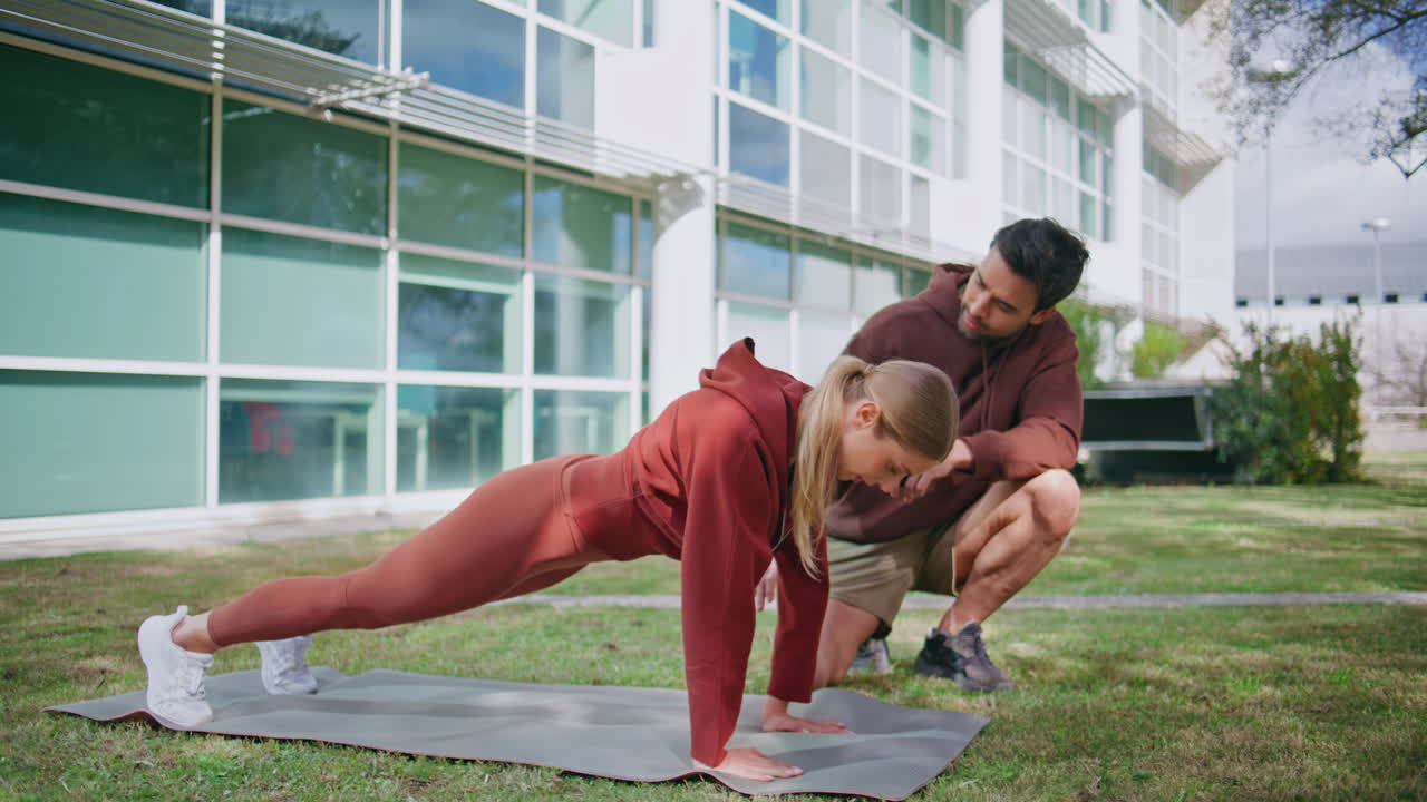 Man coaching plank exercise in city park. Focused woman doing sport exercise