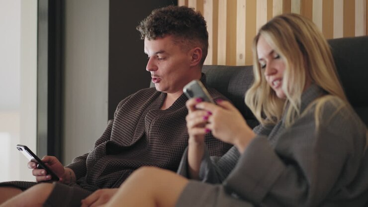 una coppia innamorata sta trascorrendo il fine settimana nel complesso termale un uomo e una donna si rilassano nella sala relax e navigano su internet con lo smartphone