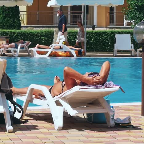 personas sentadas a la orilla de la piscina de un resort durante las vacaciones de verano