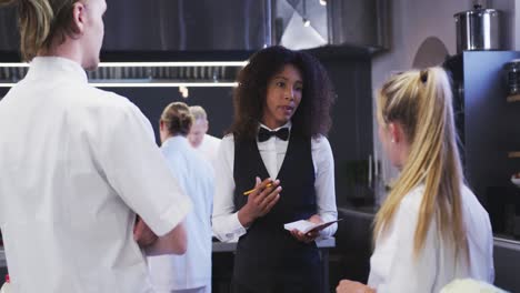 gerente de restaurante afroamericana en la cocina dando instrucciones al cocinero caucásico