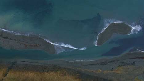 aerial view of waves crashing ashore and around small islands below a mountain view in iceland