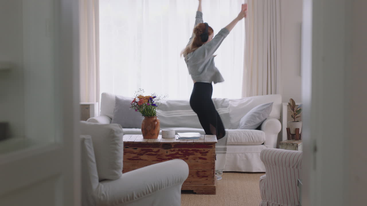 행복한 여성이 집에서 춤을 추고 재미있게 음악을 듣고 헤드폰을 착용하고 재미있는 춤 동작으로 주말 축제를 즐기고 있습니다.