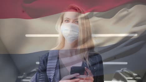 Animation-of-flag-of-netherlands-waving-over-woman-wearing-face-mask-during-covid-19-pandemic