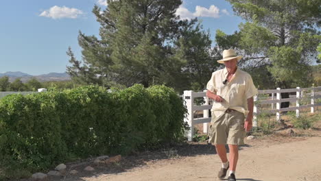 Older-man-with-hat-and-cigar-walks-in-foot-cast-due-to-broken-toe,-outside-nature-park-environment