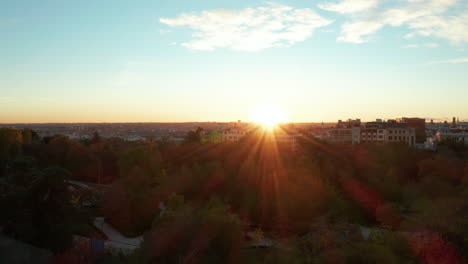 Rising-footage-of-housing-estate-against-setting-sun.-Rays-of-bright-sun-making-lines.-Fly-above-trees-in-public-park.