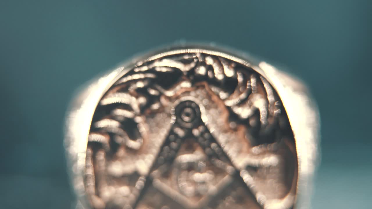 un macro detallado plano inclinado hacia arriba de un anillo masónico de textura dorada, en un soporte reflectante, símbolo de illuminati, iluminación de estudio profesional, video 4k