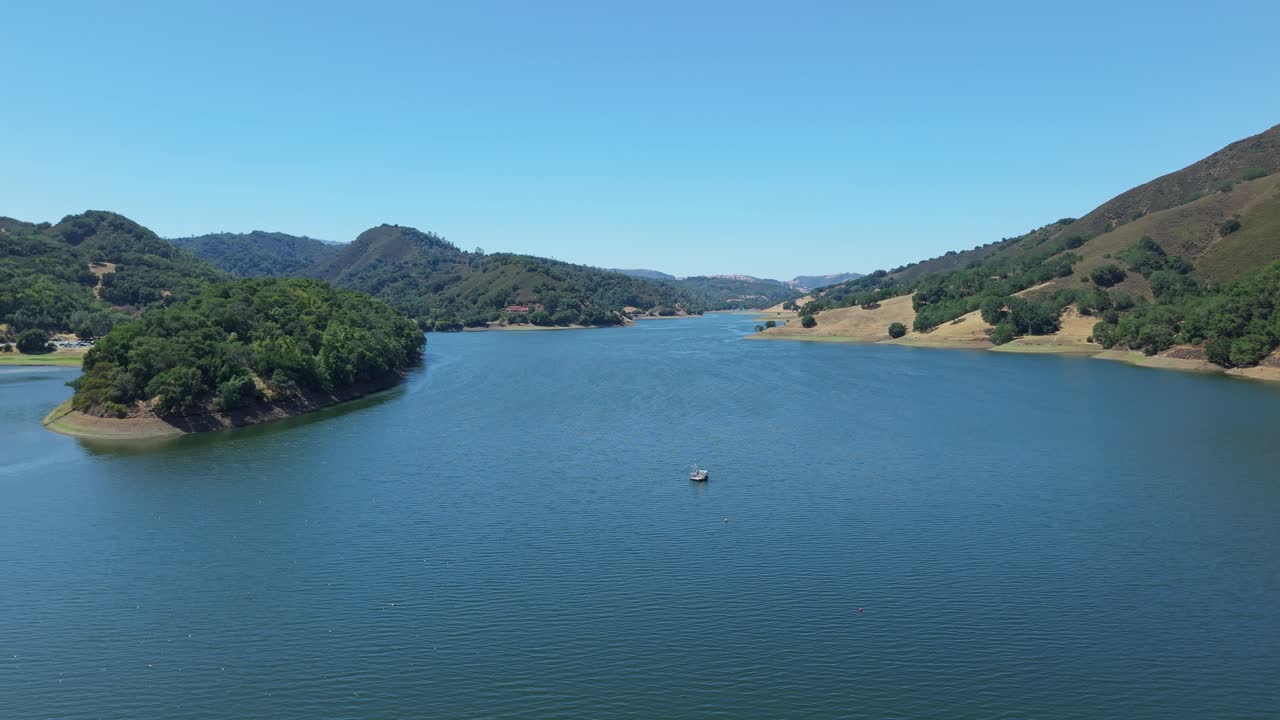 The reservoir's curves stretch outward, nestled between ridges and meadows in this graceful overhead sweep