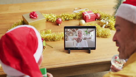 padre y hijo caucásicos con sombreros de santa usando una tableta para una videollamada de navidad con una mujer en la pantalla