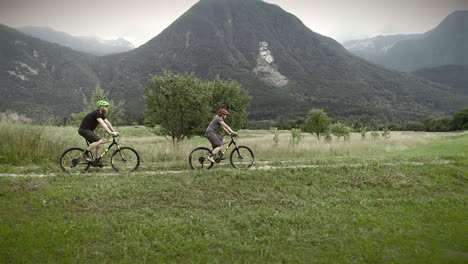 aerial view of a couple driving mountain bikes on dirt road surrounded by hills.